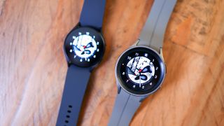 Två stycken Samsung Galaxy Watch 5 ligger med urtavlorna vända uppåt på ett trägolv.