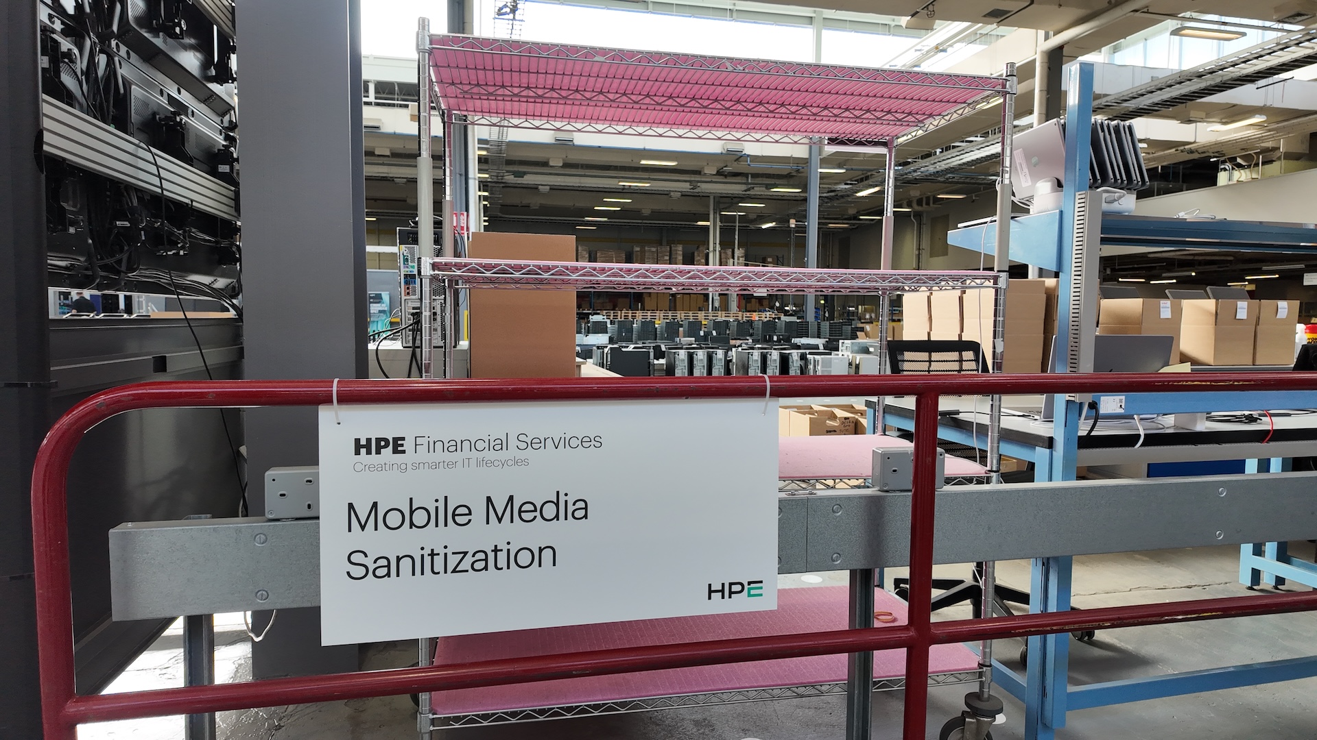 A sign reading 'mobile media sanitization' hangs on a red fence with steel shelves behind it.