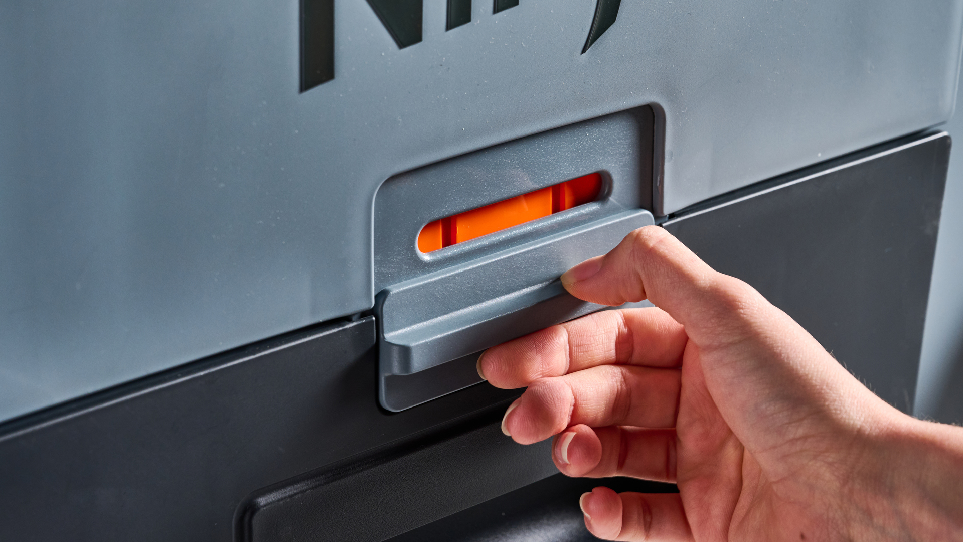 The dry tray latch of the Ninja FrostVault 45QT Wheeled Cooler photographed in front of a blue background.