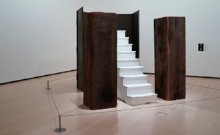 Inside an exhibition area is a white staircase surrounded by brown wooden blocks.