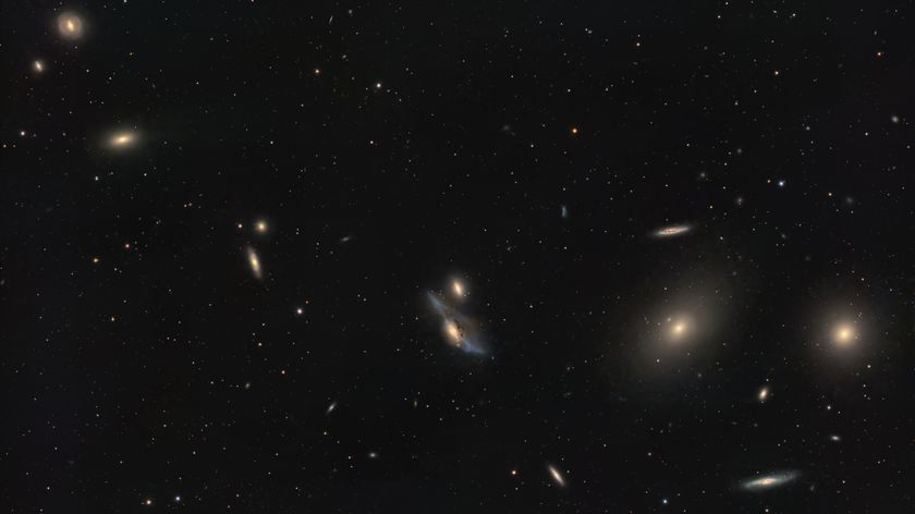 A string of galaxies shines in a deep space photo in a black sky dotted with stars.