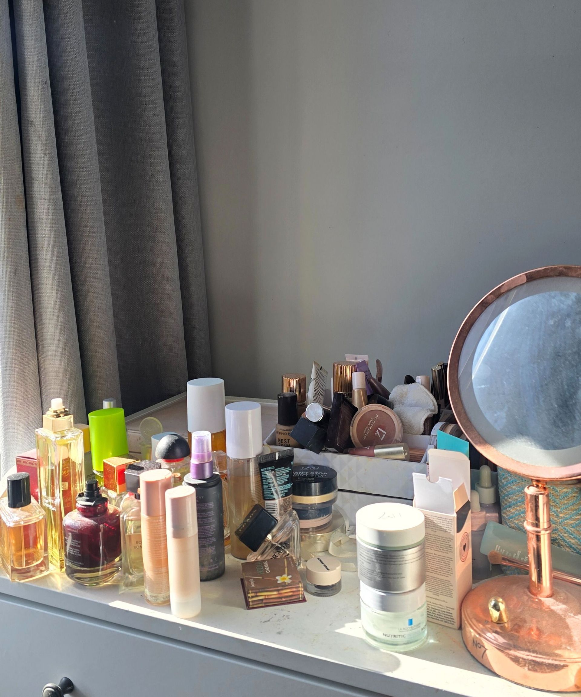 An untidy vanity with perfume bottles, makeup, jewelry, and boxes on top of it