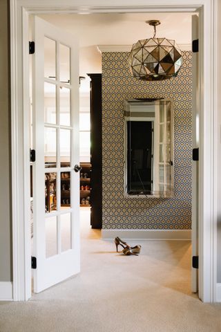 walk in closet with French style doors, wallpaper, shoes to one side, vintage silver pendant light, carpet