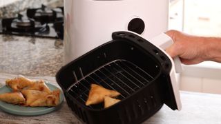 Someone removing the basket from an airfryer illustrating What you need to know before buying an air fryer
