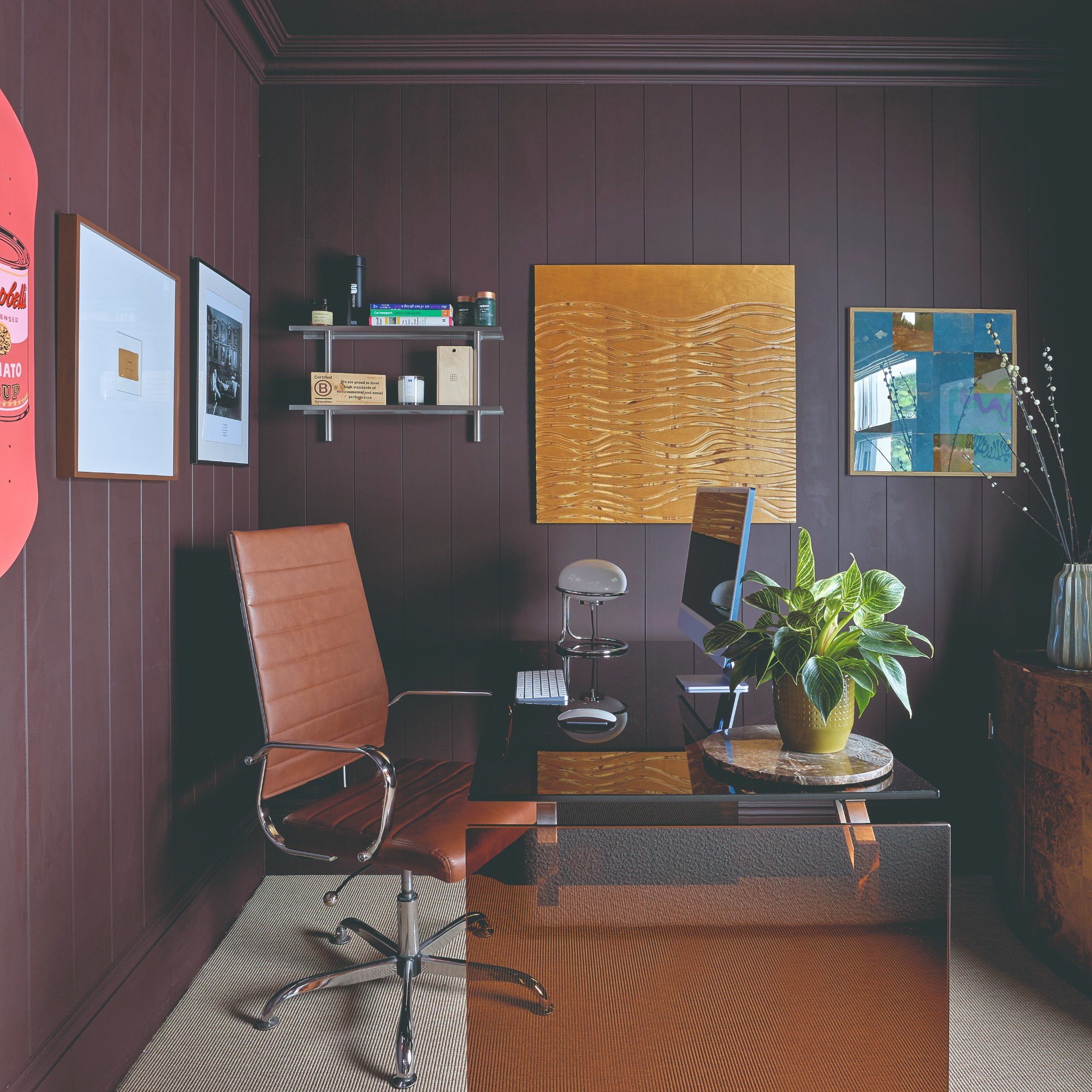 An aubergine purple-painted home office with wall panelling and art hung on the walls, with one of the frame being extra sizes compared to the artwork within
