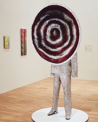 mannequin dressed in silver in an art gallery with a large red and white target covering the head and torso