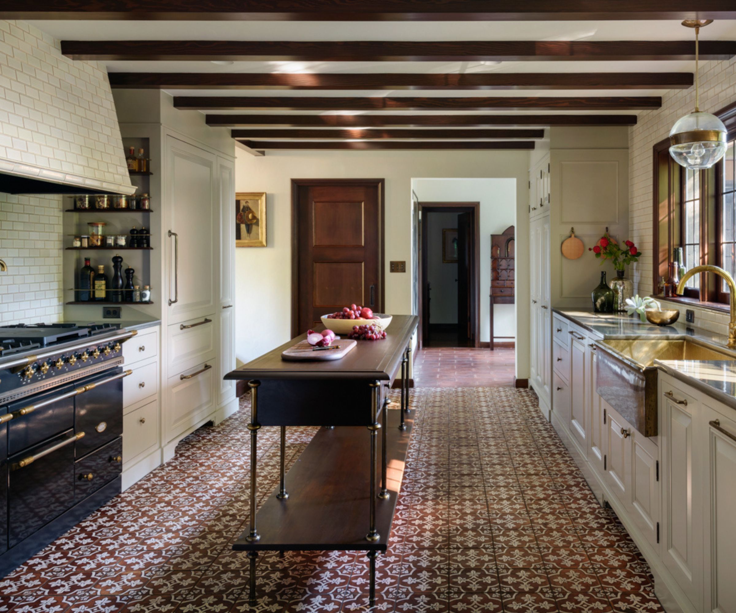 Tudor kitchen with dark beams, tiled floor, subway tiled hood and range oven and cream cabinets
