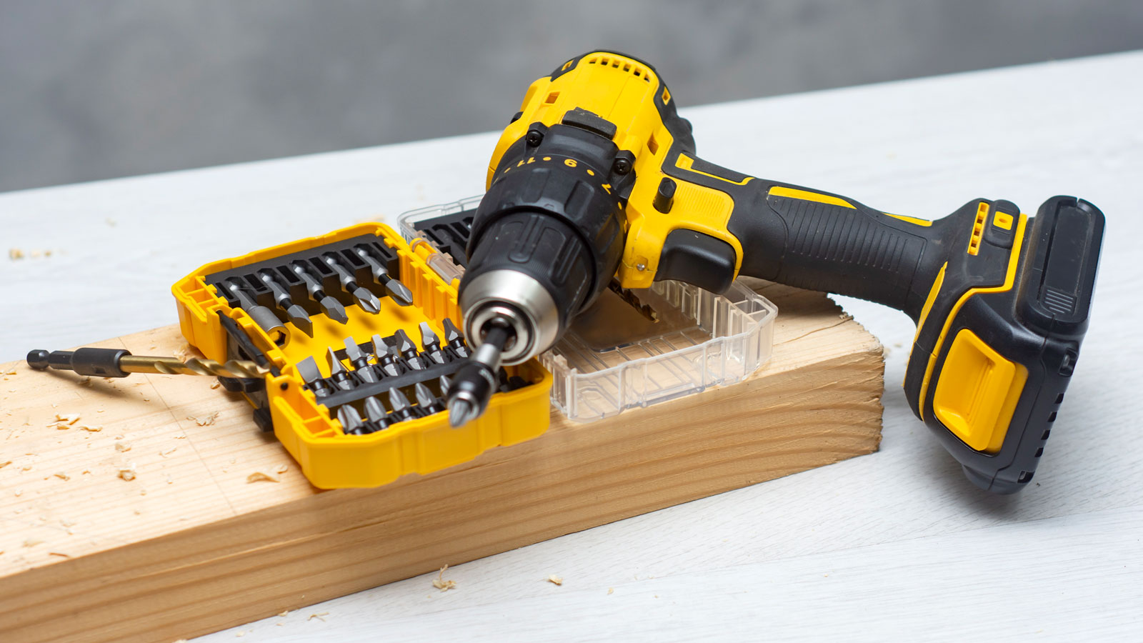 Yellow cordless drill on top of box of screwdriver bits on wood and table