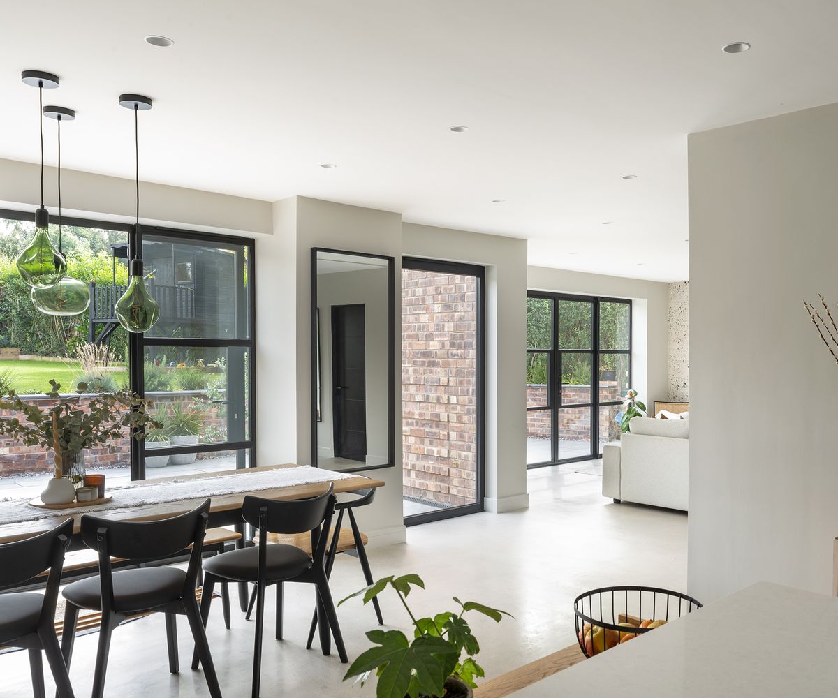 A bright and airy home extension shwing a dining table to the left and a view of a lounge area to the far right of the shot. There is plenty of contemporary glazing incorporated into the design with large glass doors which open out onto a patio. The floor is a light polished concrete