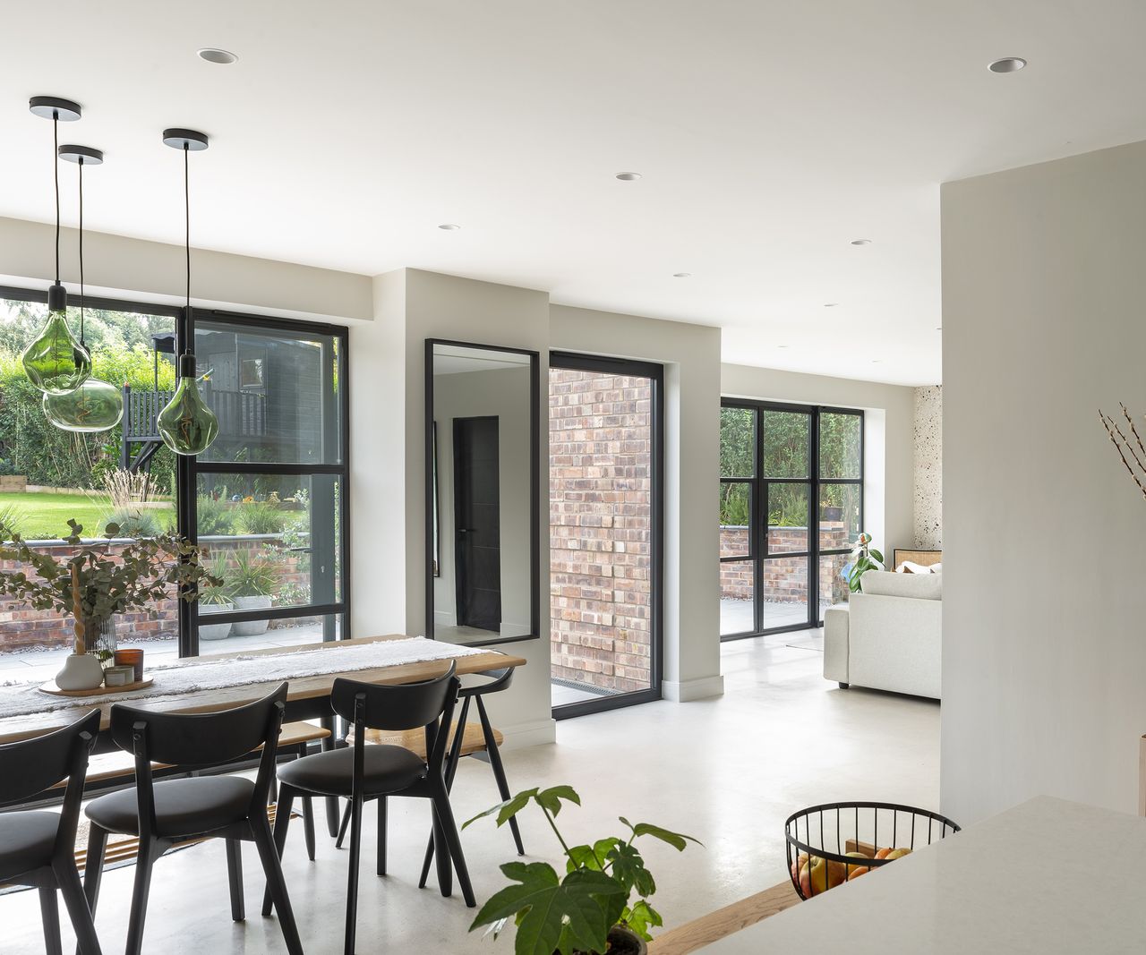 A bright and airy home extension shwing a dining table to the left and a view of a lounge area to the far right of the shot. There is plenty of contemporary glazing incorporated into the design with large glass doors which open out onto a patio. The floor is a light polished concrete