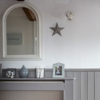 White and grey hallway with grey radiator with cover against wall with candles, vase and framed picture on top of it