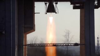 close-up of a rocket engine firing on a test stand, generating a pillar of orange flame