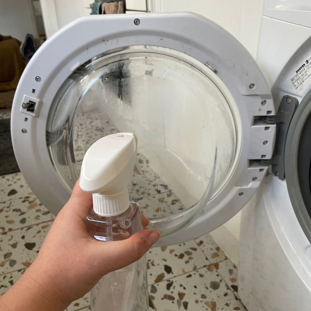 Holding a spray bottle of vinegar up to the inside door of a washing machine