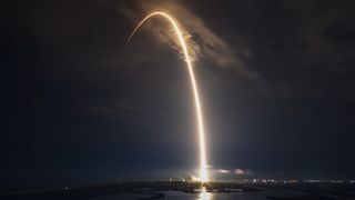 a rocket launches at night, creating an arc of light
