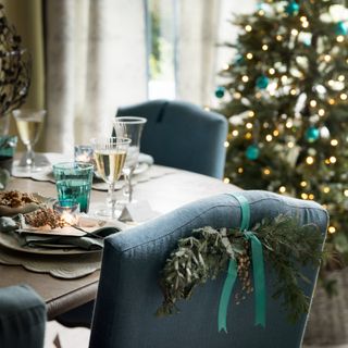 A dining table set for a Christmas dinner with scalloped placemats and lit Christmas tree in the background