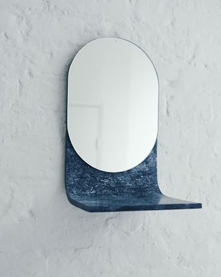 Oval shaped mirror mounted against a wall with a marble structure