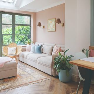 A light pink-painted living room with a cream modular sofa adorned with multicolouredf cushions