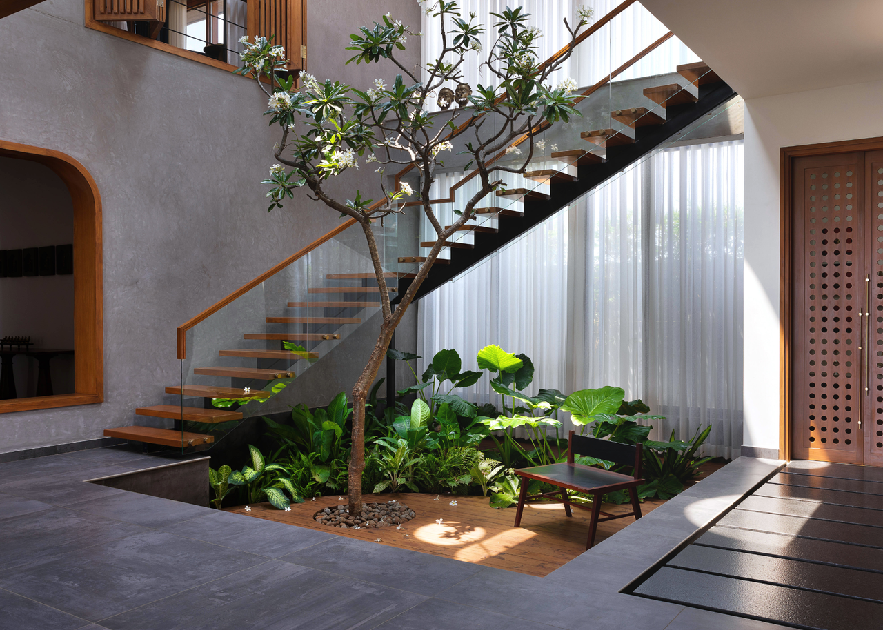An Earthy Indian home with a courtyard garden with a bench, a frangipani tree and a staircase around