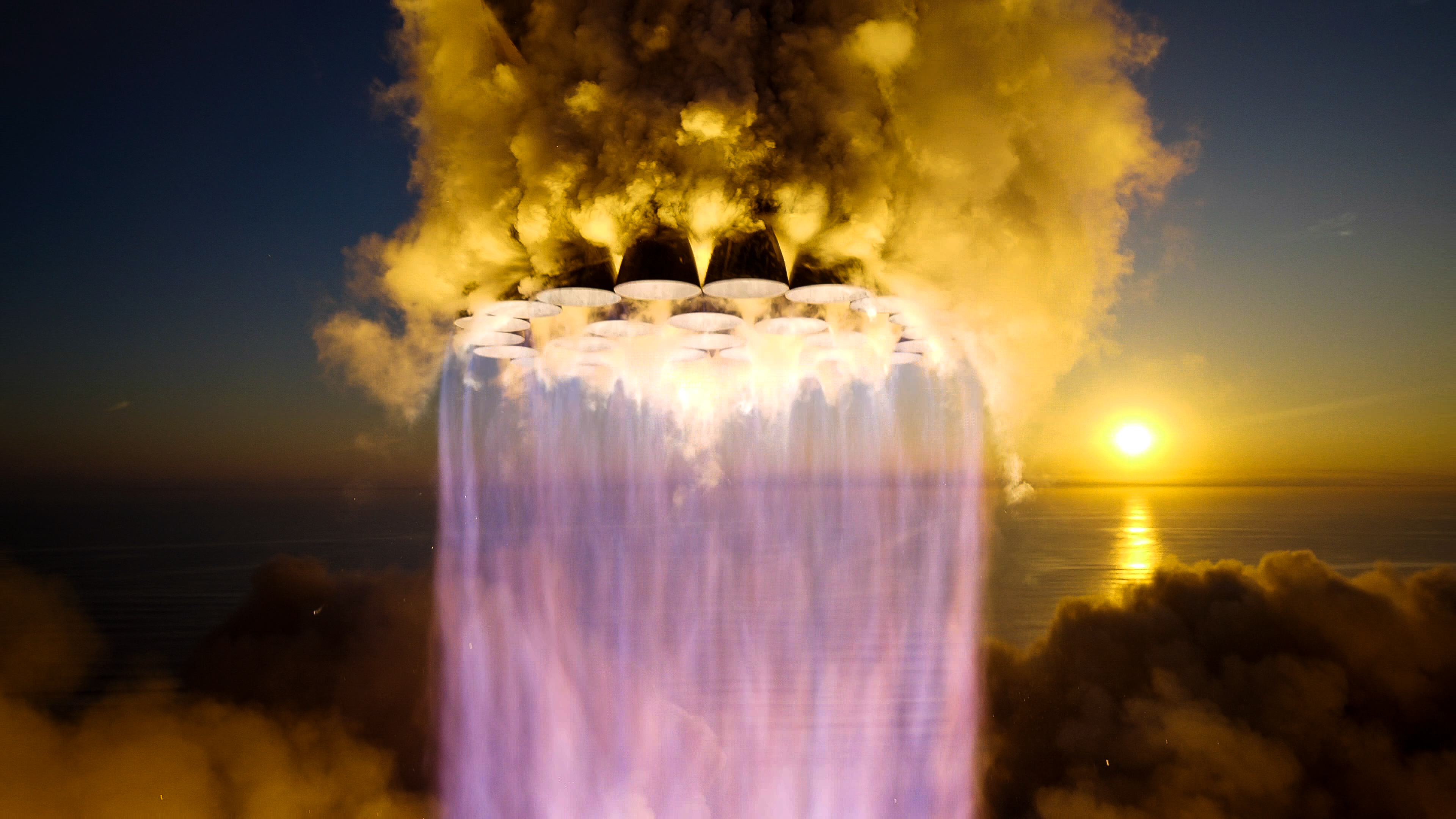 close-up shot of all 33 of the first-stage engines of SpaceX's Starship first stage burning as the vehicle rises off the launch pad, with a rising sun in the background.