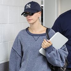 Hailey bieber wears a yankees hat, gray sweatshirts, black shorts, white socks and navy suede miu miu sneakers.
