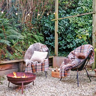 Gravel area in garden with industrial fire pit and two chairs with blankets