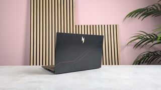 Rear of Acer Nitro V 15 open on desk with wooden panels, plant, and pink wall in background