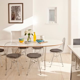 white dining room with oval table, modern wire chairs, yellow and turquoise tableware, artwork, pale wood laminate tiles