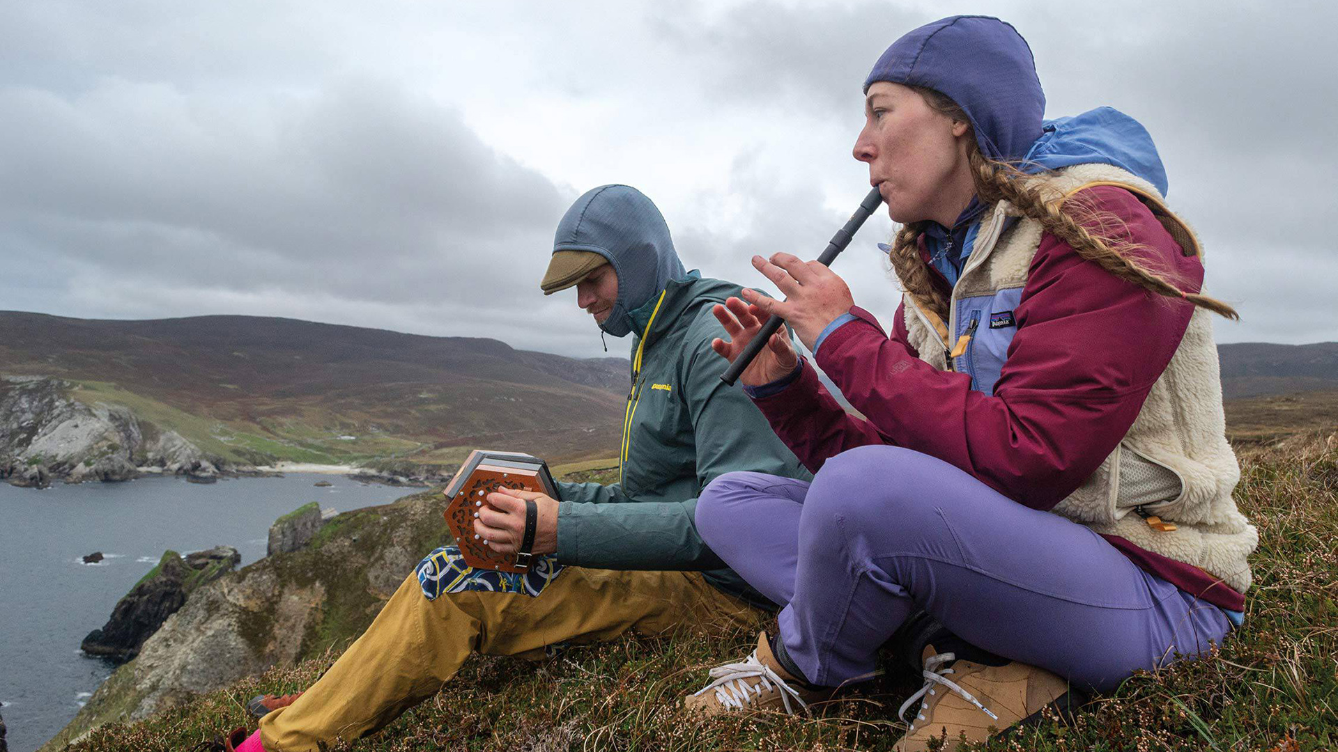 Two hikers playing instruments on a hill wearing head-to-toe Patagonia gear