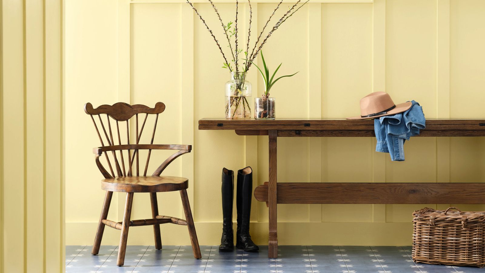 a panelled entryway painted in a sunshine yellow with a rustic wooden bench, vintage wooden chair, boots, and vases of foliage