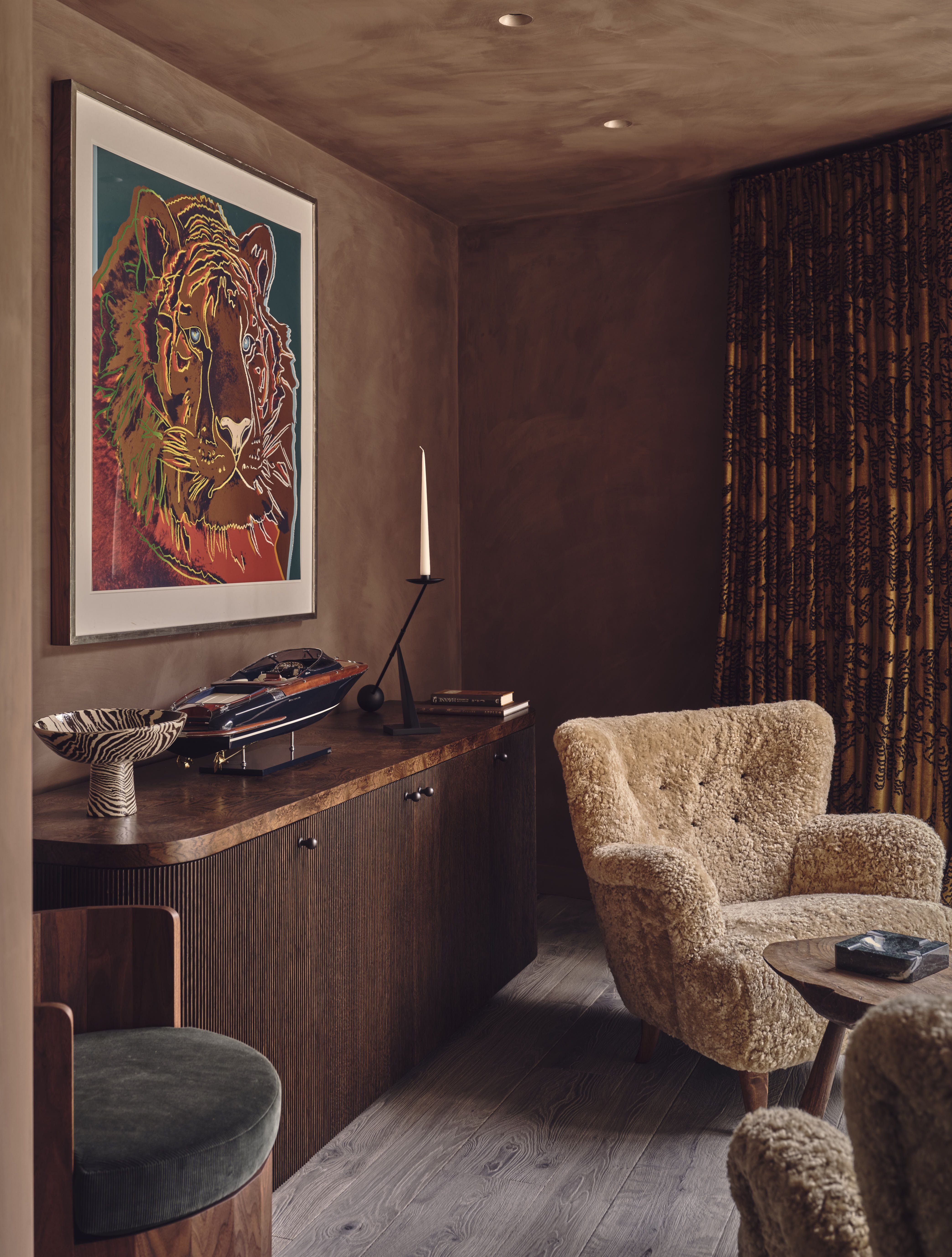 cigar room with hazelnut plaster on the walls and ceiling, teddy chair, console with candlestick, henry holland bowl, large artwork, and patterned curtains