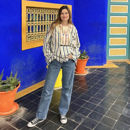 French editor and writer Eugenie Trochu poses in a Bohemian chic looks with an embroidered striped tunic, jeans, and black Converse sneakers