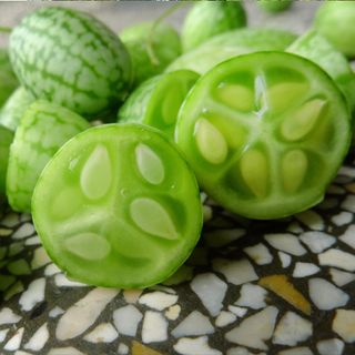 A close-up on several cucamelons, one of which has been cut in half to show the seeds within