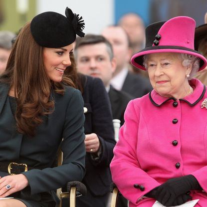 Princess Kate sitting next to Queen Elizabeth wearing a pink suit and smiling