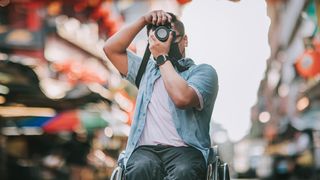 Male photographer in a wheelchair taking photos in a city street