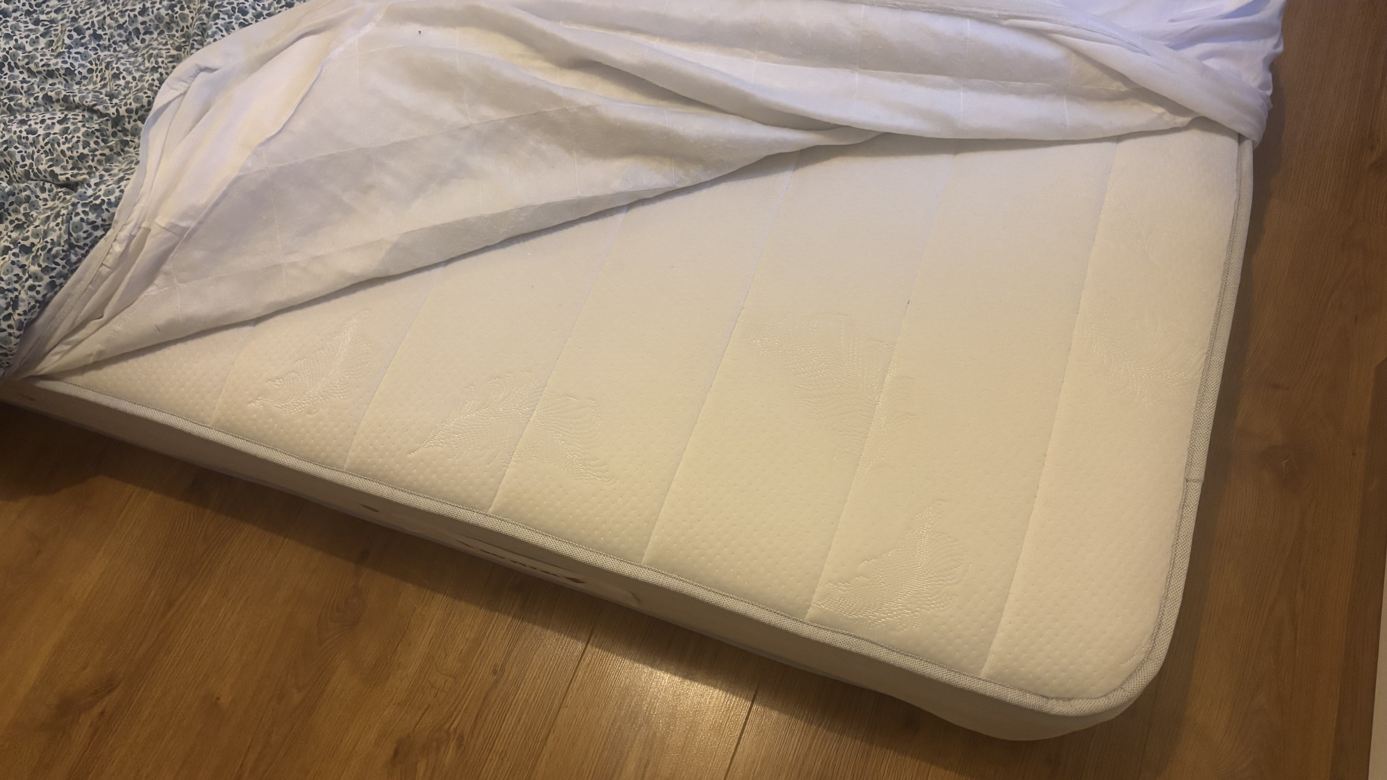 A spring mattress on the floor dressed in floral bedding.