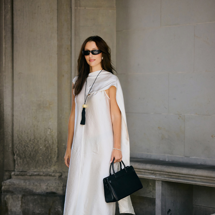 woman wears white dress with black handbag and tassel. 