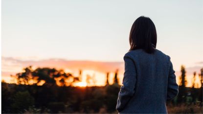 Woman looking at sunset in distance wearing jacket