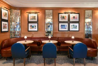 An old Hollywood-style restaurant features brown and blue leather seating, mirror accents, and bistrot-style wall art.