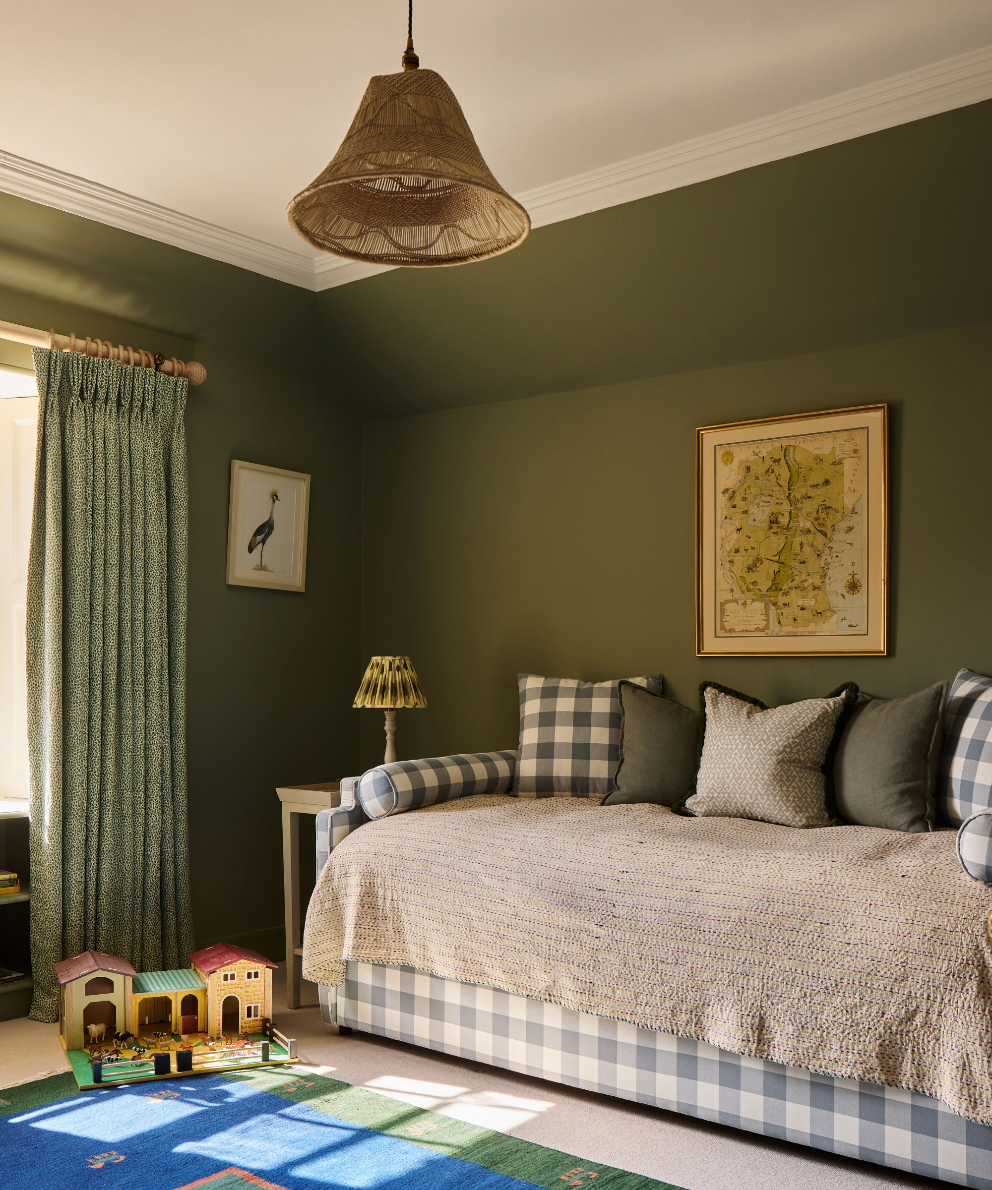 Olive green bedroom featuring a blue-and-white gingham daybed, patterned green curtains, and a woven wicker pendant light overhead