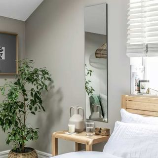 Sage green bedroom with a large frameless mirror on the wall beside the bed above a bedside table 