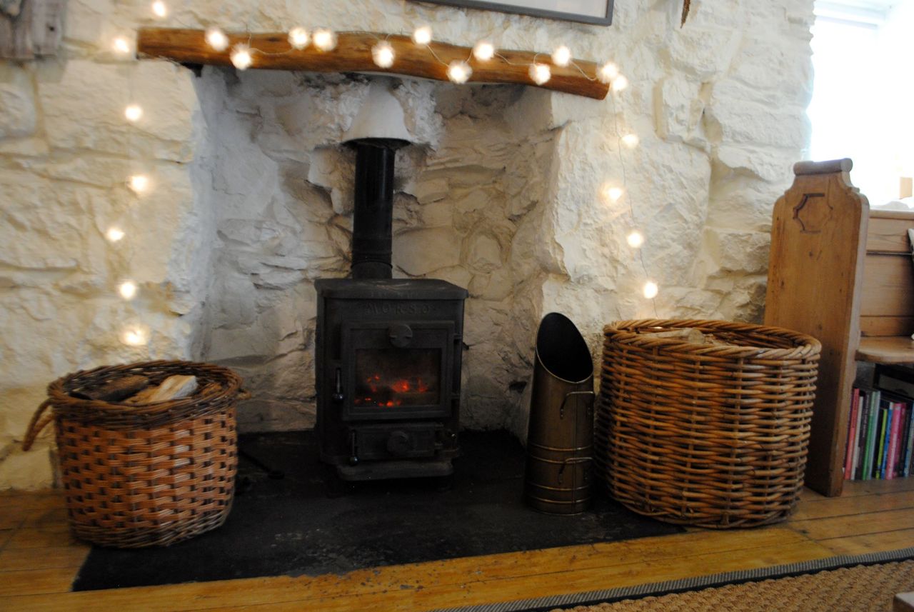 The wood burner has a black exterior and has white stone walls around it and wooden flooring beneath
