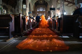 Gemma Winter and Chesney Brown walking down the aisle with a huge orange wedding dress train following behind her