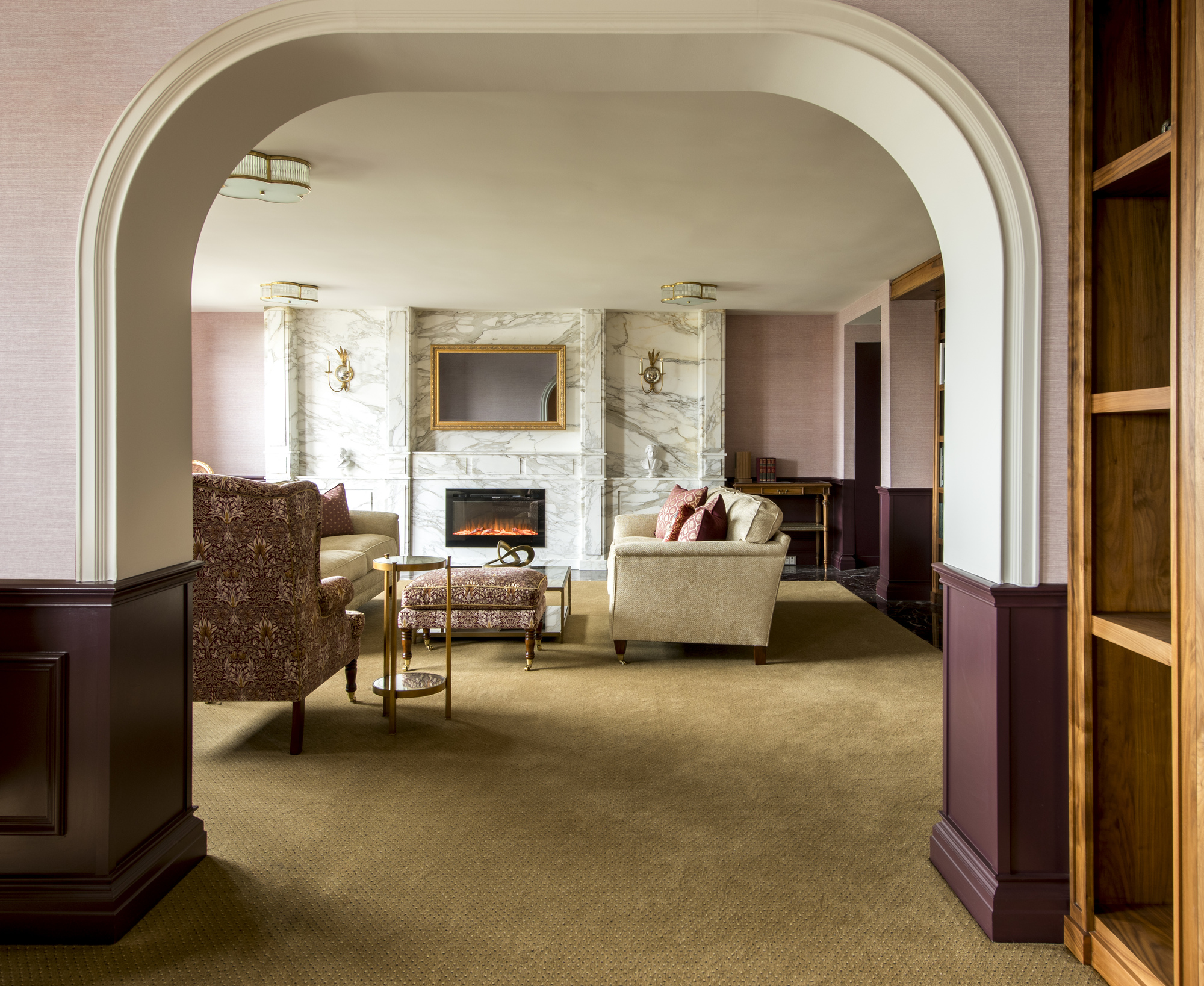 elegant living room with pale pink walls, burgundy details, caramel carpets, a marble fireplace, and patterned armchairs