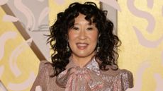 Sandra Oh pictured with a medium haircuts with bangs, a curly shag, on a yellow backdrop