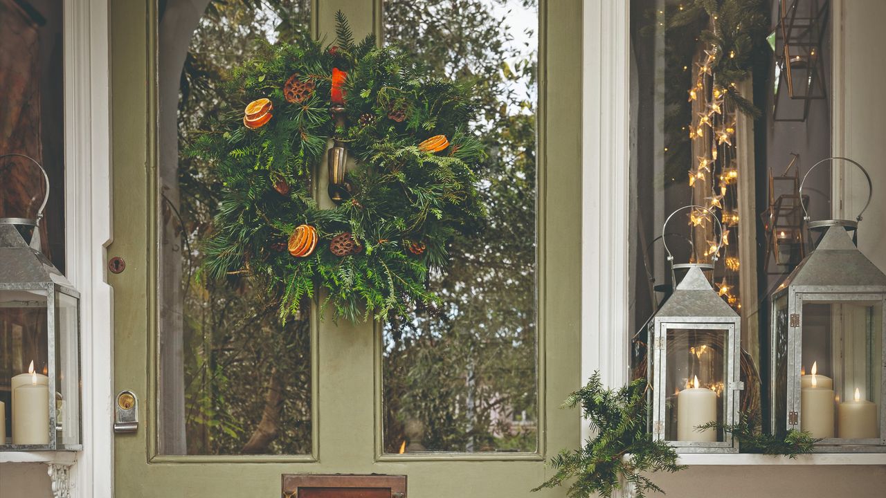 A sage green front door decorated with a Christmas wreath