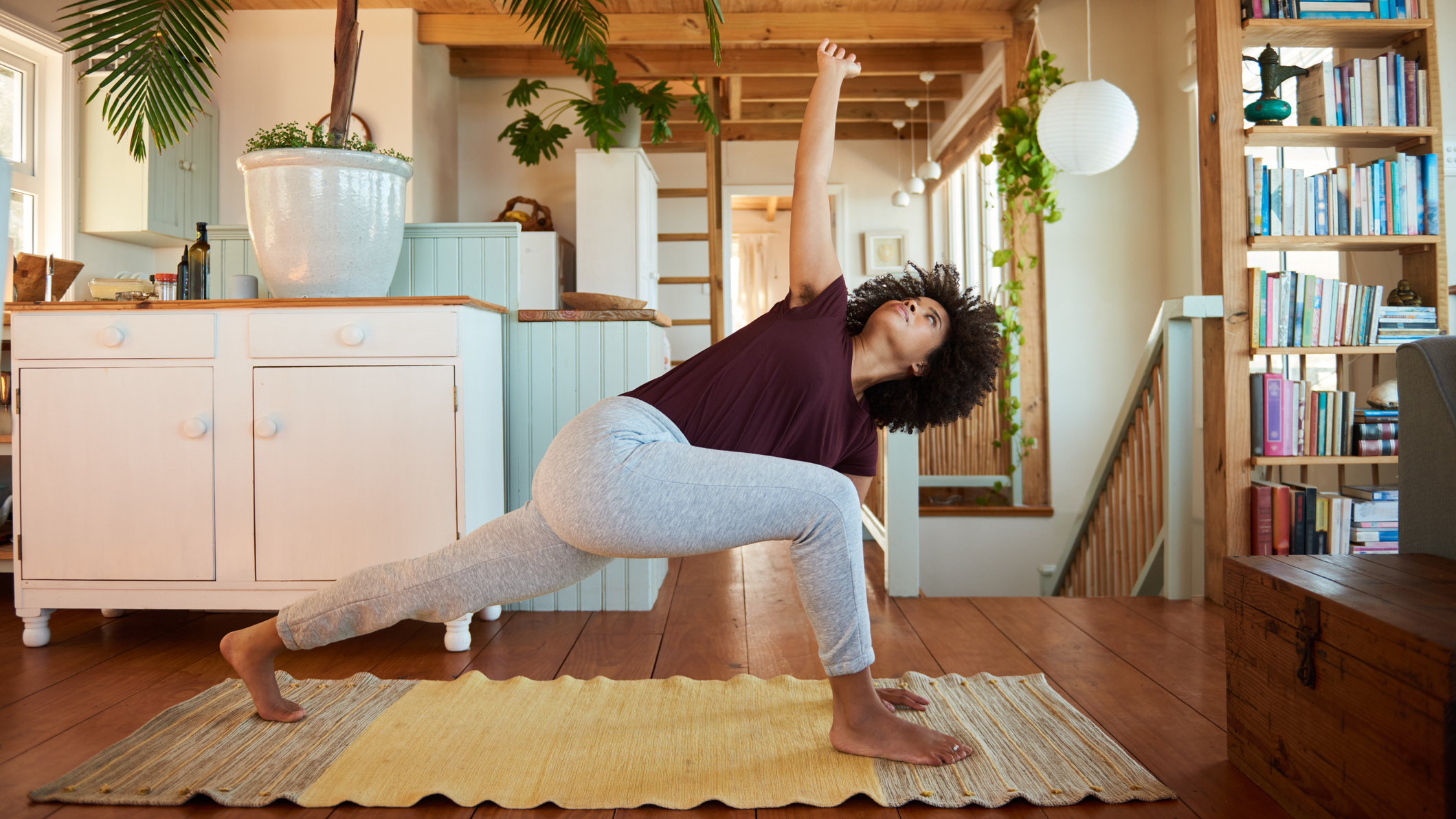 Woman practicing yoga at home, with her left foot behind her, her left hand and right foot in front of her and her right hand pointing up