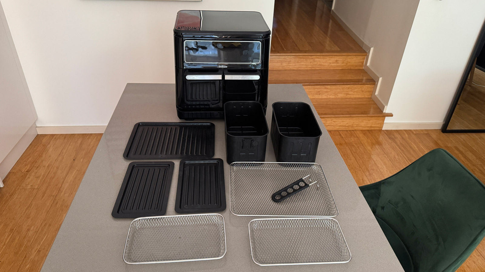 Sunbeam Multi Zone Air Fryer Oven on kitchen counter top, with its six cooking trays and two cooking baskets laid out in front of it