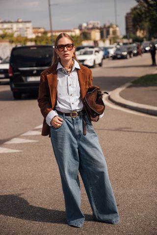 woman wearing suede jacket, button-down shirt, jeans, and heels