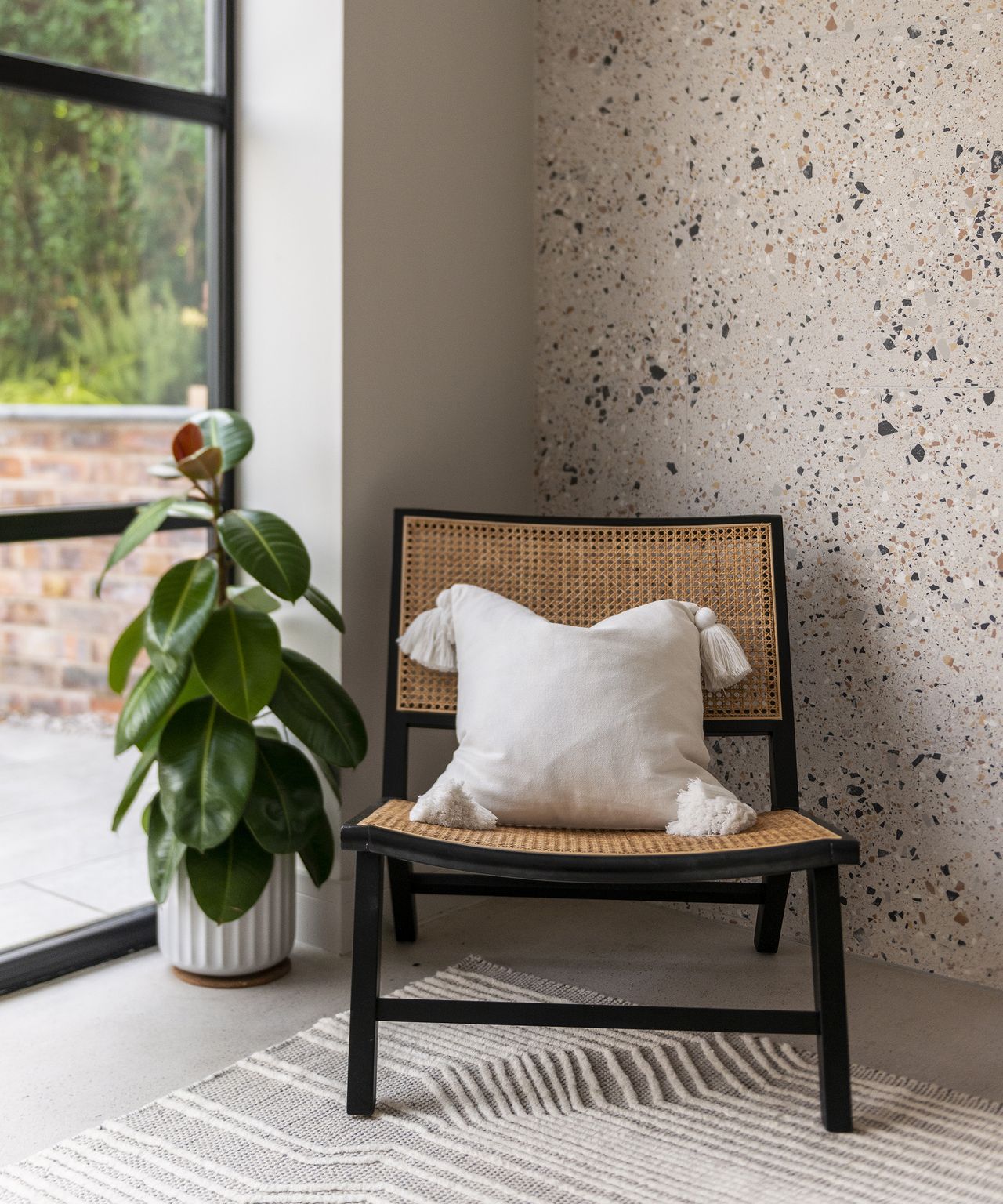 A statement wicker chair in the corner of an open plan extension. The wall is covered in terrazzo style