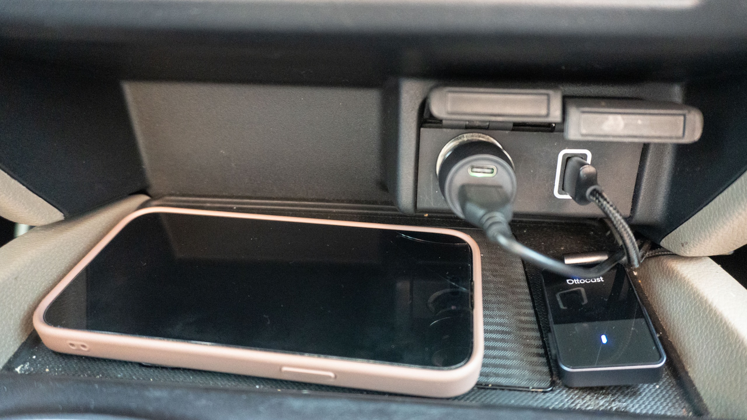 A phone charging on a wireless charging pad next to the Ottocast OttoSafe Cam's wireless adapter plugged into a car's USB port